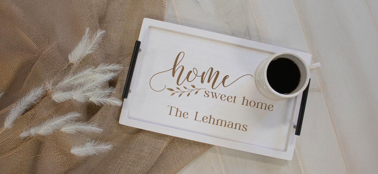 White serving tray with "home sweet home" engraved on it with a coffee mug on top