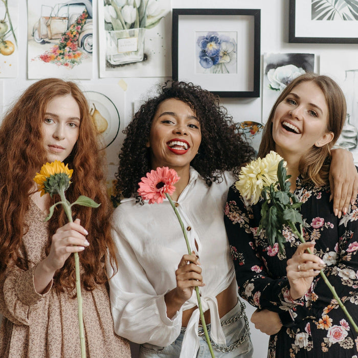 Three women smiling while holding flowers