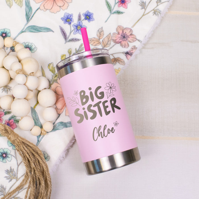 small pink kids tumbler laying on a floral blanket with decorative beads engraved with big sister and floral accents