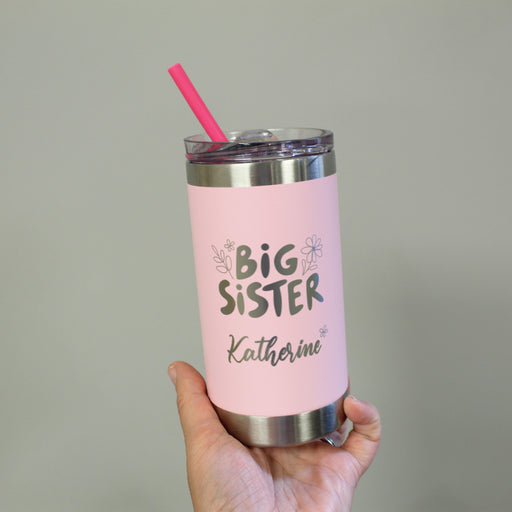 Pink tumbler with 'Big Sister' text held by a hand against a neutral background