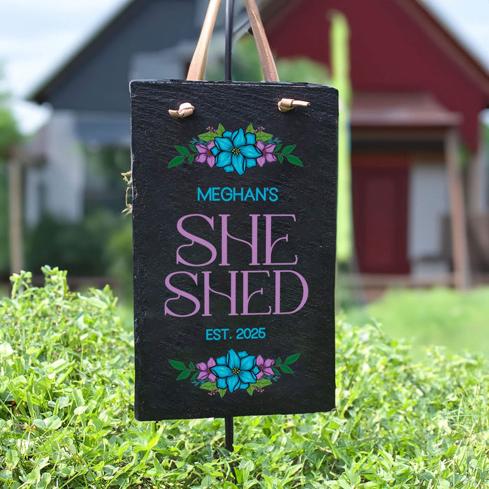Personalized 'SHE SHED' sign with floral designs on a grassy background