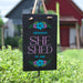 Personalized 'SHE SHED' sign with floral designs on a grassy background