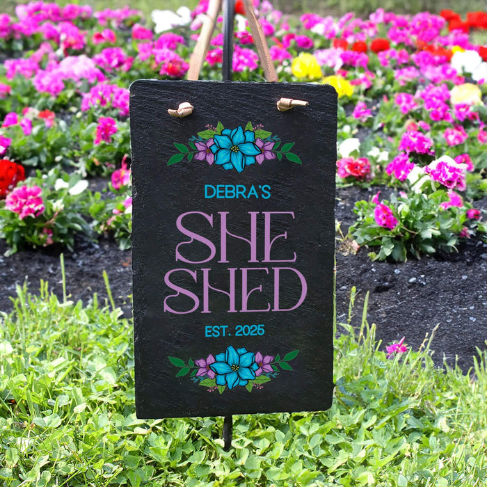 Personalized 'SHE SHED' sign with floral designs in a garden setting