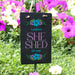 Decorative sign with 'Laura's She Shed' text in a garden setting with pink flowers