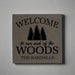 gray vegan leather wall sign engraved  with 'Welcome to our neck of the woods' text and tree graphics on a gray background.