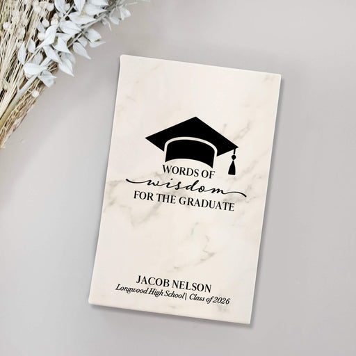 Graduation-themed journal with a marble cover and engraved text on a gray surface.