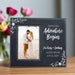 Personalized photo frame with a couple on a beach and engraved text, placed on a wooden surface with flowers in the background.