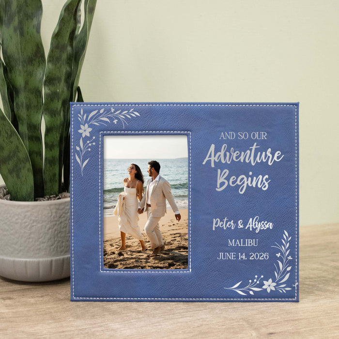 Personalized photo frame with couple on beach and text 'And so our adventure begins' on a wooden surface with a plant in the background.