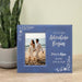 Personalized photo frame with couple on beach and text 'And so our adventure begins' on a wooden surface with a plant in the background.