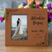 Personalized photo frame with a couple on a beach and engraved text, placed on a wooden surface with flowers in the background.