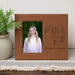 Brown leather photo frame with engraved text and a photo of a young woman, placed on a surface with a plant in the background.