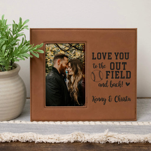 Brown leather photo frame with a couple's photo and engraved text on a wooden surface.