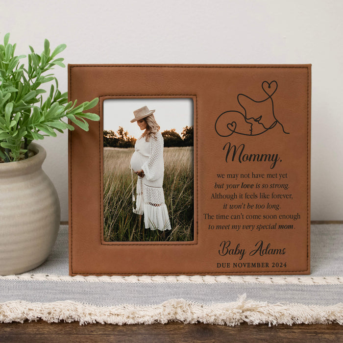 Brown leather picture frame with a photo of a pregnant woman, text, and a plant on a surface.