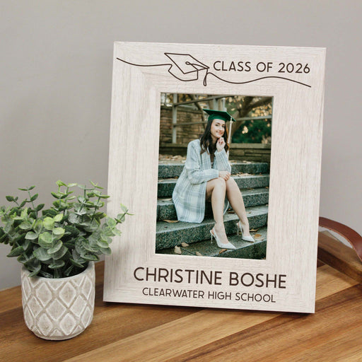 Graduation-themed photo frame with a picture of a graduate and personalized text on a wooden surface.