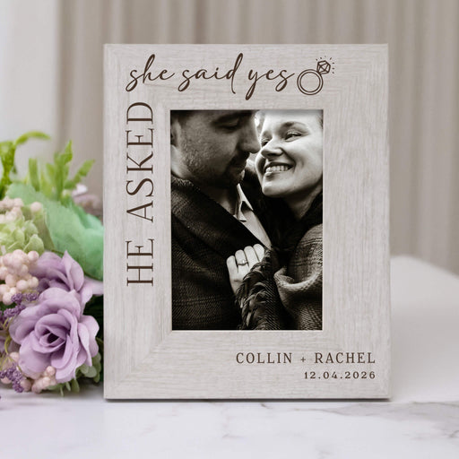Personalized photo frame with 'she said yes' text and a couple's photo, surrounded by flowers.