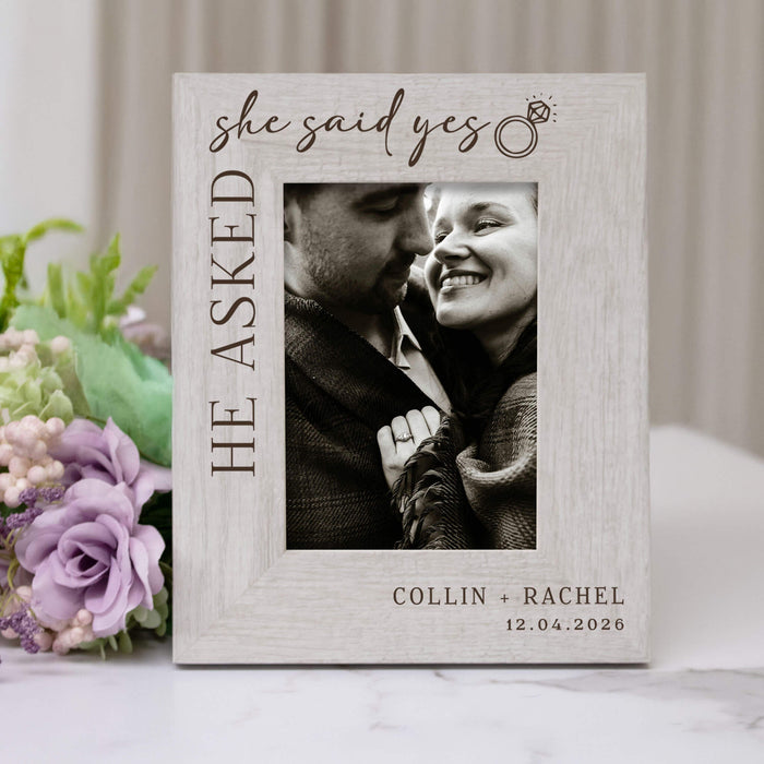 Personalized photo frame with 'she said yes' text and a couple's photo, surrounded by flowers.