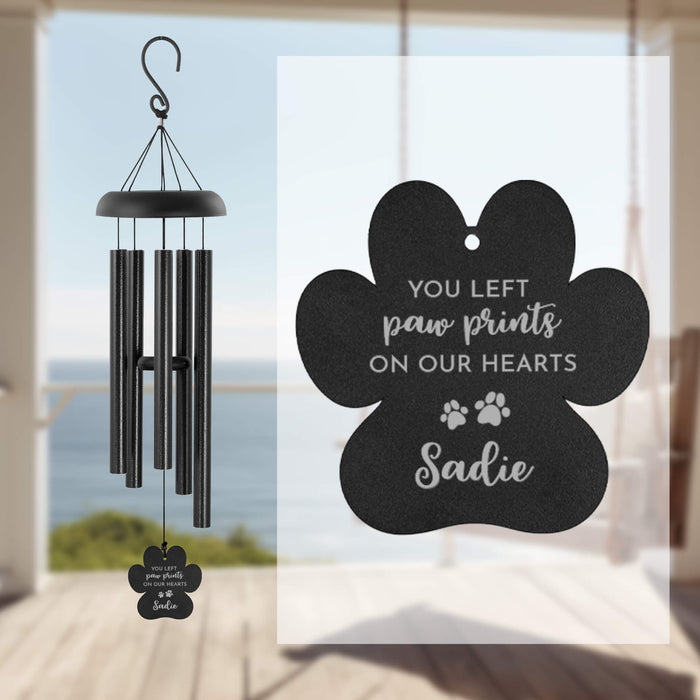 Black paw-shaped wind chime with engraved text on a beach background
