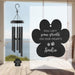 Black paw-shaped wind chime with engraved text on a beach background