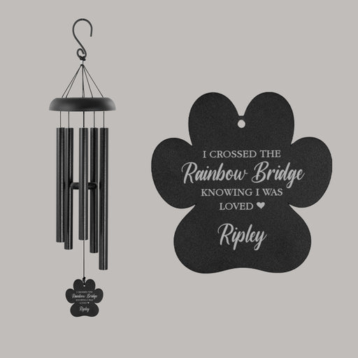 Black paw print shaped wind chime with "I crossed the rainbow bridge knowing I was loved" engraved as well as the pet's name hanging in front of a gray background