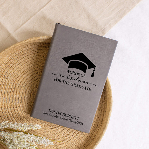 Gray journal engraved with 'Words of Wisdom for the Graduate' with a graduation cap design on a woven mat