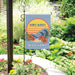 Garden flag with 'Don't Worry, Beach Happy' text and wave design in a garden setting.
