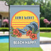Decorative garden flag with 'Don't Worry, Beach Happy' text and floral design on a stake by the pool.
