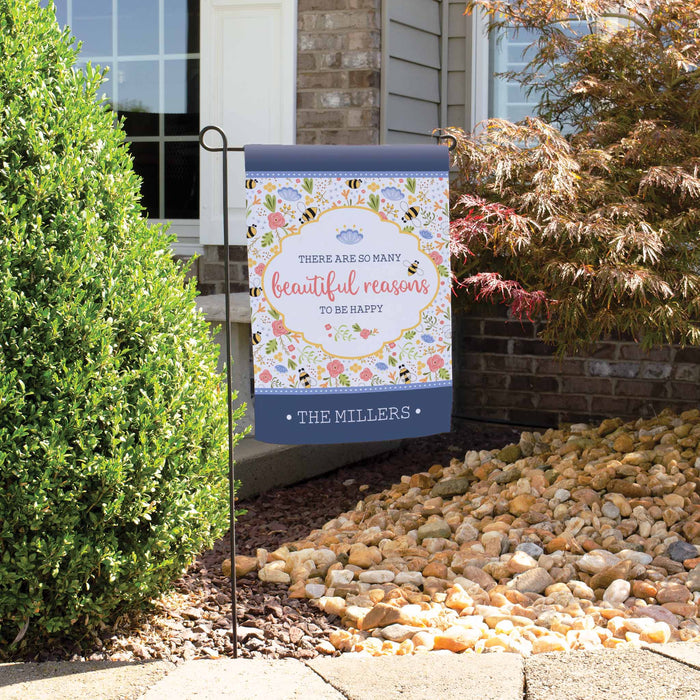 Decorative garden flag with motivational quote and family name in front of a house.