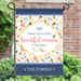 Decorative garden flag with floral design and motivational quote on a stand outdoors.