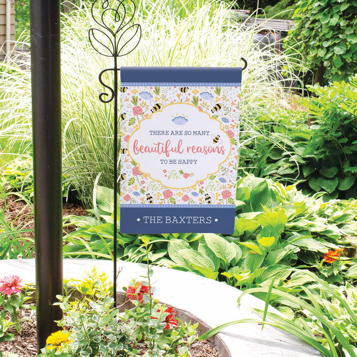 Decorative garden flag with 'The are so many reasons to be happy' quote in a garden setting