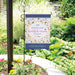 Decorative garden flag with 'The are so many reasons to be happy' quote in a garden setting