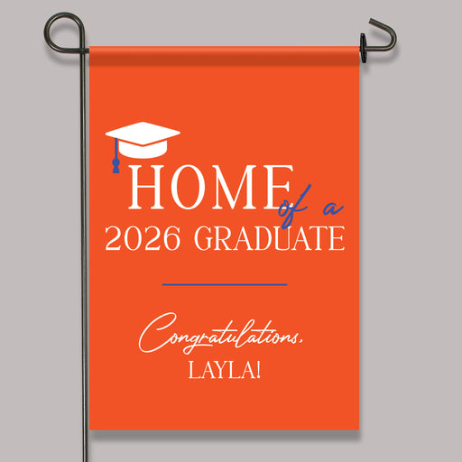 Orange garden flag with 'Home of a 2026 Graduate' text and graduation cap design on a gray background.