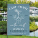 Garden flag with 'Last Toast on the Coast' design, featuring a cocktail and beach elements, set against a blurred outdoor background.