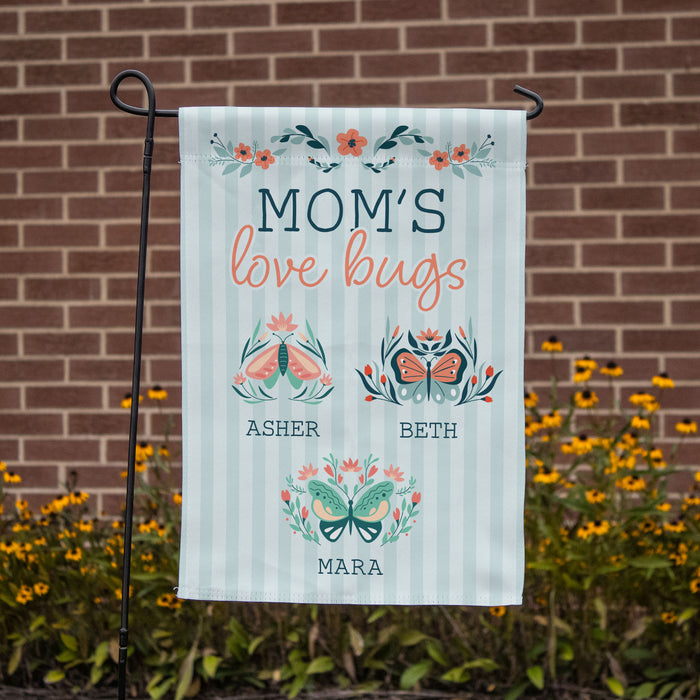 blue striped yard flag that has three different butterflies for each child's name in front of a brick wall and yellow flowers