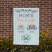 blue striped yard flag that has three different butterflies for each child's name in front of a brick wall and yellow flowers