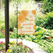 Decorative garden sign with orange design and text in a garden setting