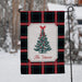 A personalized holiday garden flag hanging from a black metal stand in a snowy outdoor setting. The flag features a black and red plaid pattern with a central white label containing a green Christmas tree illustration and the text 'The Vances'.
