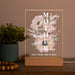 Decorative lamp with floral design and text on a wooden base, next to a plant and beads.