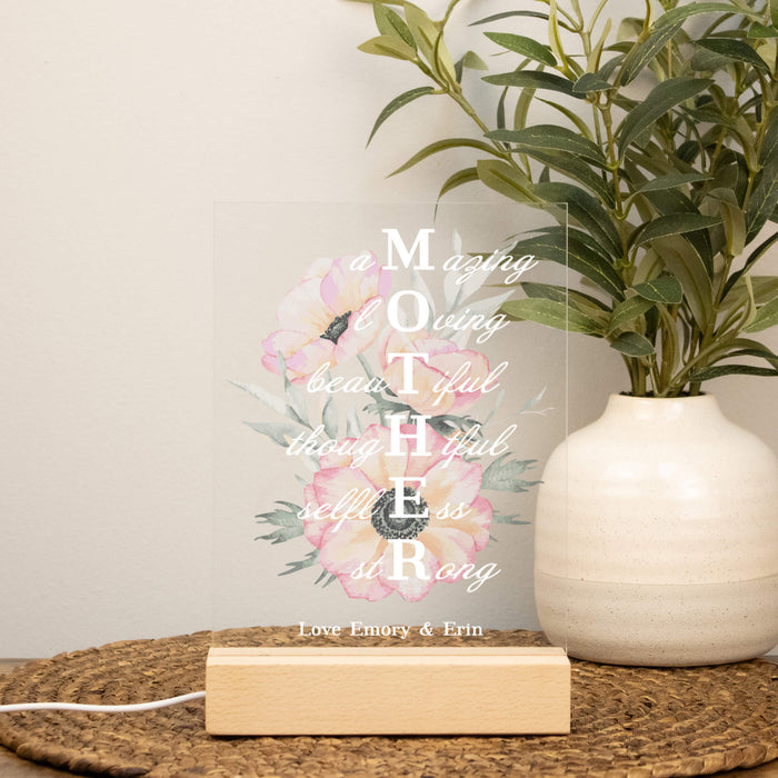 Decorative sign with floral design and text on a table with a plant in the background