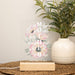 Decorative sign with floral design and text on a table with a plant in the background