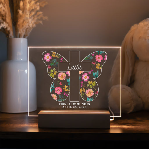 Decorative LED sign with floral cross design and personalized text on a wooden surface.