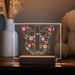 Decorative LED sign with floral cross design and personalized text on a wooden surface.