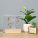 Butterfly-shaped floral design with personalized text on a wooden stand next to a potted plant.