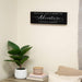 Decorative wall sign with personalized text above a plant and books on a shelf.