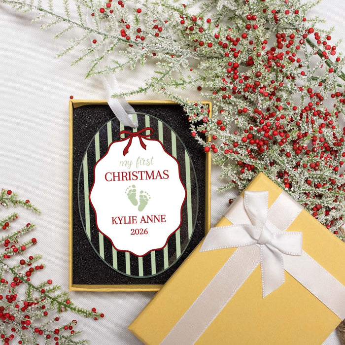 A personalized Christmas ornament, displayed in its gift box on a white fabric background with festive red berries and a yellow gift box with a white ribbon.