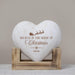 A heart-shaped white wood plaque with a brown engraved Christmas design and the text 'BELIEVE IN THE MAGIC OF Christmas' and the name 'Isabella', displayed on a small wooden stand against a neutral beige background.