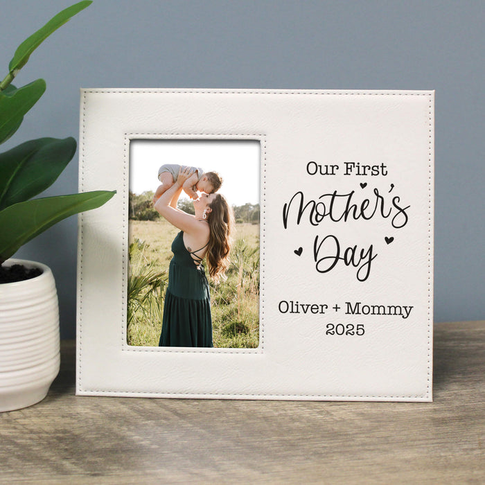 White photo frame with a picture of a woman holding a child and text 'Our First Mother's Day Oliver + Mommy 2025' on a wooden surface.