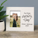 White photo frame with a picture of a woman holding a child and text 'Our First Mother's Day Oliver + Mommy 2025' on a wooden surface.