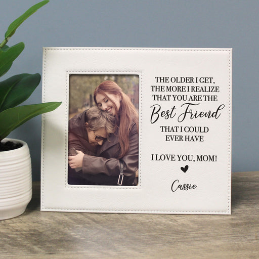 White photo frame with a picture of two people and a message to a mother, on a wooden surface with a plant.