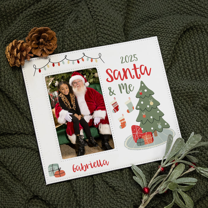 A personalized Christmas photo frame styled on a dark green chunky knit blanket with pinecones and holly. The white frame features a photo of Santa, festive text reading '2025 Santa & Me' and 'Gabriella', and holiday illustrations including a Christmas tree, stockings, and gifts.