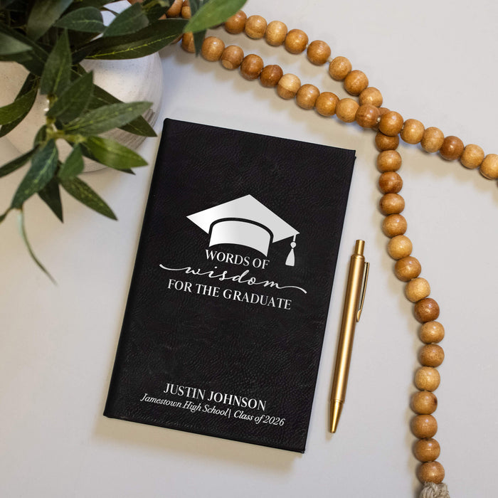Graduation-themed book titled 'Words of Wisdom for the Graduate' with a pen and beads on a light surface.